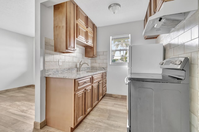 kitchen with sink, white refrigerator, washer / clothes dryer, decorative backsplash, and light wood-type flooring