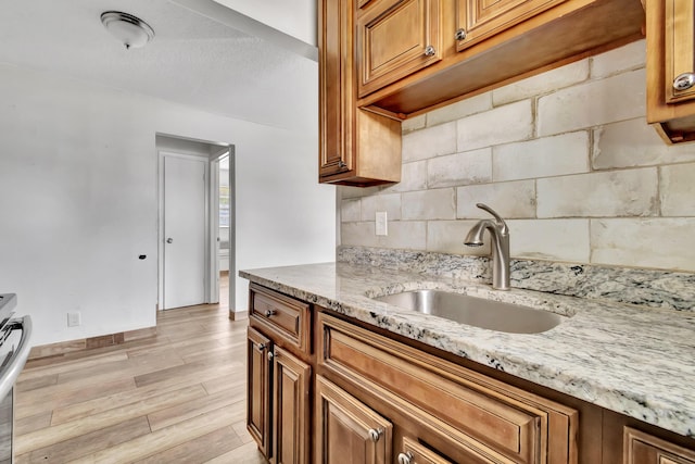 kitchen featuring a textured ceiling, light stone counters, light hardwood / wood-style flooring, and sink