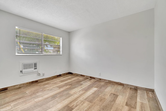 unfurnished room featuring a textured ceiling, light hardwood / wood-style flooring, and a wall mounted air conditioner