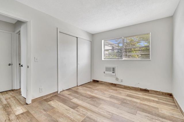 unfurnished bedroom with heating unit, light wood-type flooring, a textured ceiling, and a closet