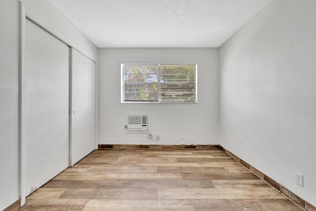 unfurnished bedroom featuring heating unit, light wood-type flooring, a textured ceiling, and a closet