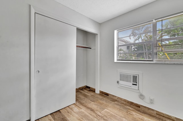 unfurnished bedroom with a closet, light hardwood / wood-style flooring, a wall mounted air conditioner, and a textured ceiling