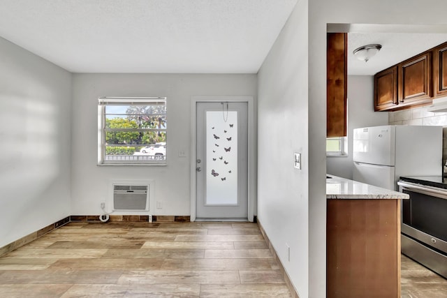 interior space featuring a wall mounted air conditioner, light hardwood / wood-style flooring, stainless steel range oven, white refrigerator, and a textured ceiling