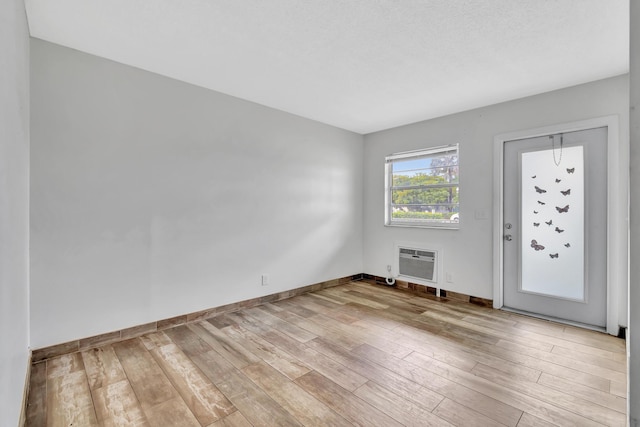 foyer with light wood-type flooring, a textured ceiling, and a wall unit AC