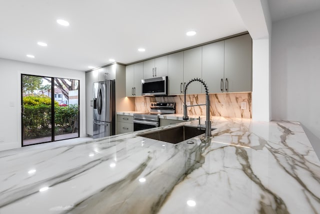 kitchen featuring gray cabinetry, light stone countertops, sink, decorative backsplash, and appliances with stainless steel finishes