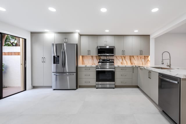 kitchen featuring light stone countertops, sink, stainless steel appliances, tasteful backsplash, and gray cabinets