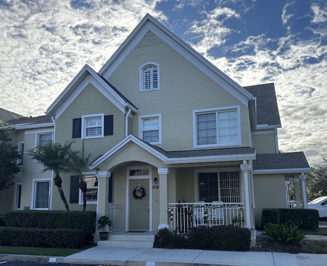 view of front of home featuring covered porch, stucco siding, and roof with shingles