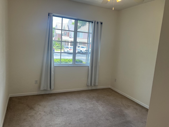 carpeted empty room featuring a ceiling fan and baseboards