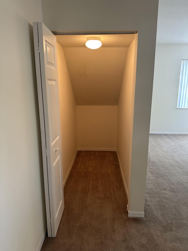 hallway with lofted ceiling, carpet, and baseboards