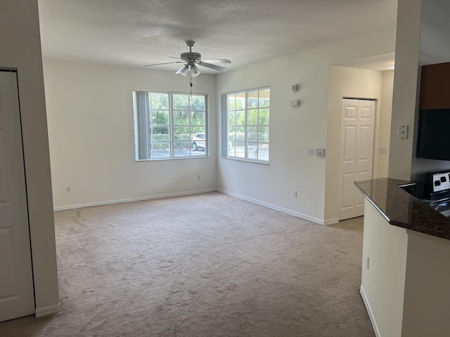 unfurnished living room featuring a ceiling fan, a textured ceiling, baseboards, and carpet flooring