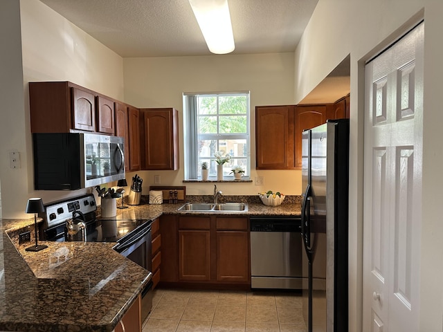 kitchen featuring light tile patterned floors, stainless steel appliances, a sink, a textured ceiling, and dark stone countertops