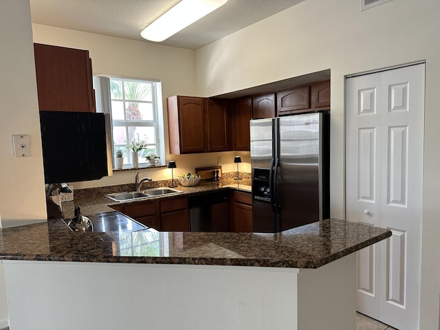 kitchen featuring a peninsula, dark stone countertops, stainless steel appliances, and a sink