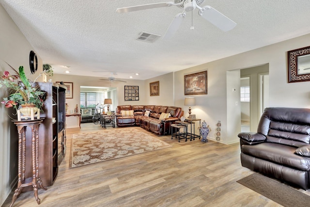 living room with ceiling fan, light wood-type flooring, and a textured ceiling