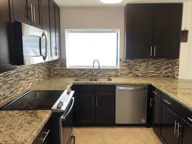 7630 Lago Del Mar Dr Unit 1, Boca Raton, FL 33433 - kitchen featuring appliances with stainless steel finishes, decorative backsplash, light stone countertops, and light tile patterned floors