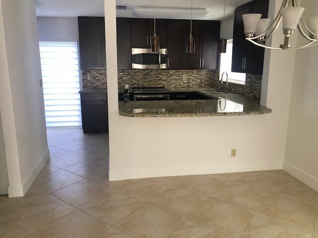 kitchen featuring appliances with stainless steel finishes, backsplash, dark stone counters, sink, and a notable chandelier