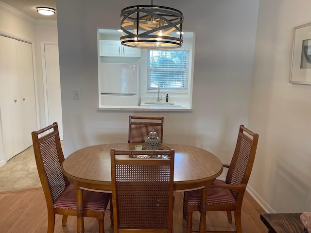 dining space with a notable chandelier, ornamental molding, sink, and light hardwood / wood-style flooring