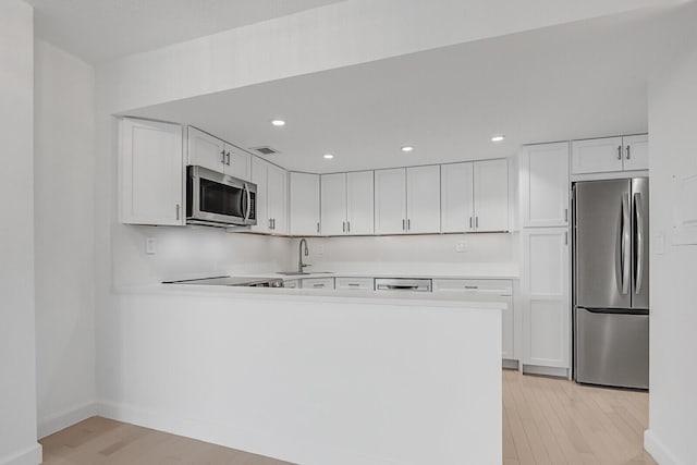 kitchen with kitchen peninsula, white cabinetry, light hardwood / wood-style flooring, and stainless steel appliances