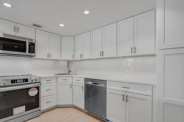 kitchen featuring sink, white cabinets, stainless steel appliances, and light wood-type flooring