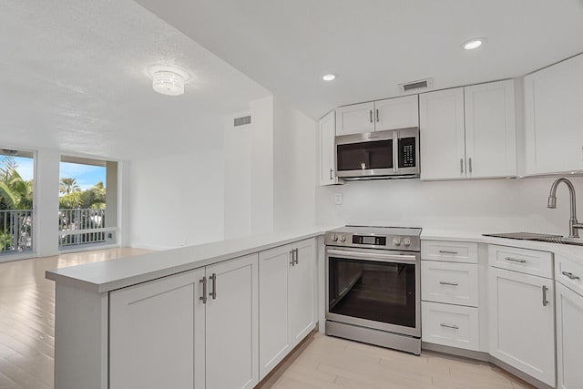 kitchen featuring kitchen peninsula, sink, light wood-type flooring, appliances with stainless steel finishes, and white cabinetry