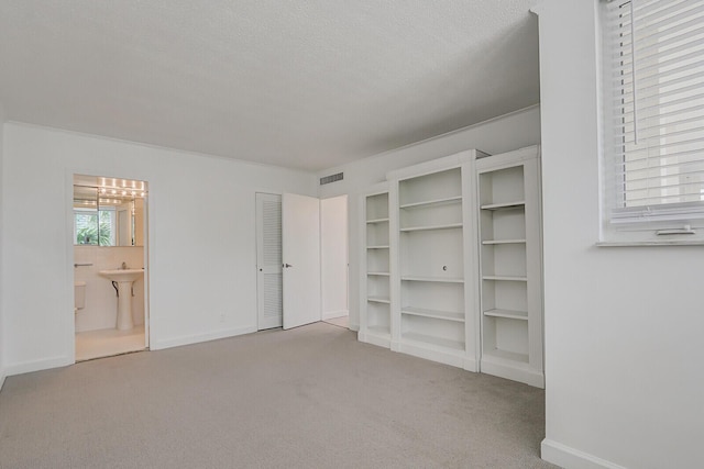 unfurnished bedroom with connected bathroom, light carpet, and a textured ceiling