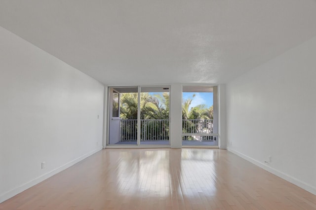 empty room with floor to ceiling windows and light hardwood / wood-style flooring