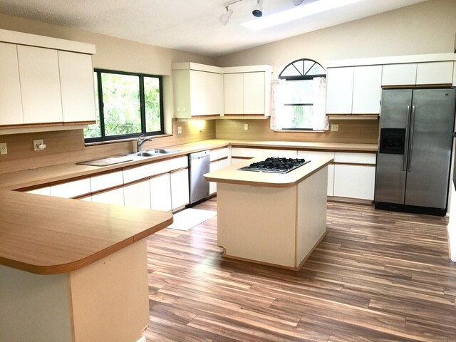 kitchen featuring white cabinets, sink, vaulted ceiling with skylight, a kitchen island, and stainless steel appliances