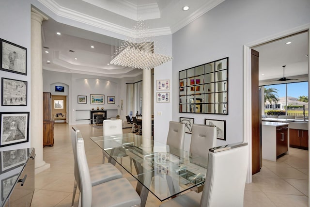 dining room featuring ornate columns, a raised ceiling, crown molding, light tile patterned floors, and ceiling fan with notable chandelier