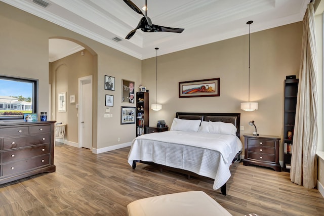 bedroom with connected bathroom, ceiling fan, a raised ceiling, light hardwood / wood-style flooring, and ornamental molding