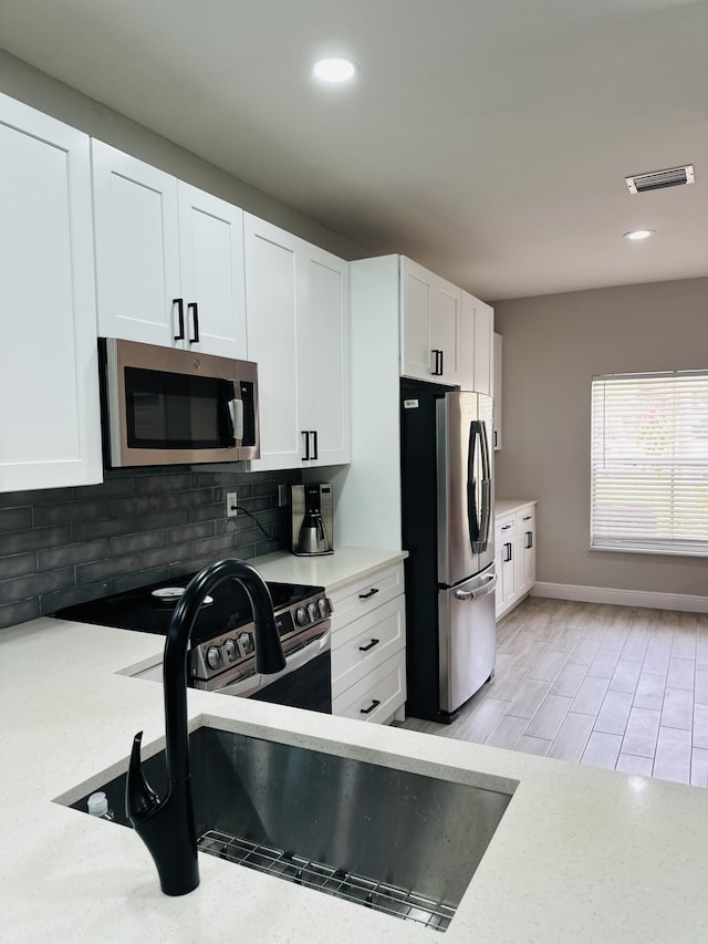 kitchen with tasteful backsplash, white cabinetry, light hardwood / wood-style flooring, and stainless steel appliances