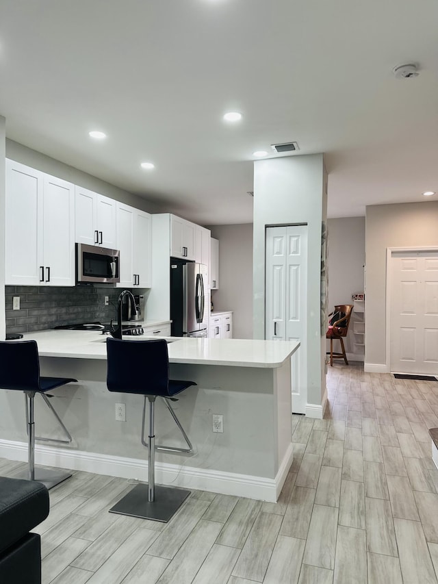 kitchen featuring kitchen peninsula, light wood-type flooring, a breakfast bar, stainless steel appliances, and white cabinetry