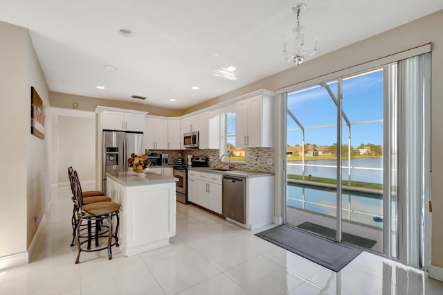 kitchen featuring stainless steel appliances, a center island, a water view, white cabinets, and decorative light fixtures