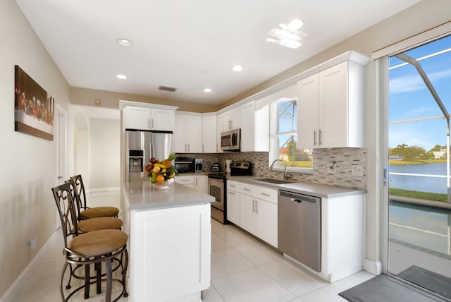 kitchen with sink, appliances with stainless steel finishes, white cabinetry, backsplash, and a kitchen bar