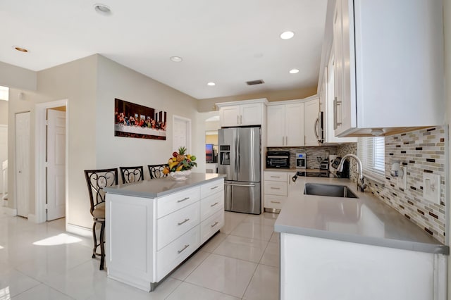 kitchen with stainless steel refrigerator with ice dispenser, a breakfast bar, sink, a center island, and white cabinets