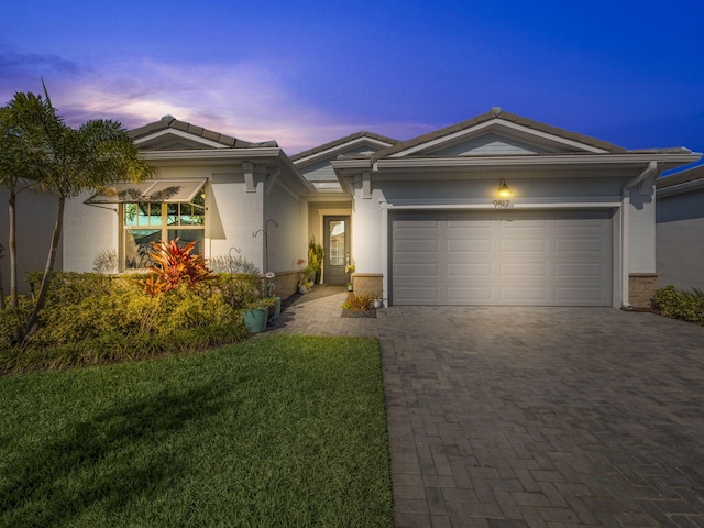 ranch-style home featuring a tile roof, an attached garage, decorative driveway, a yard, and stucco siding