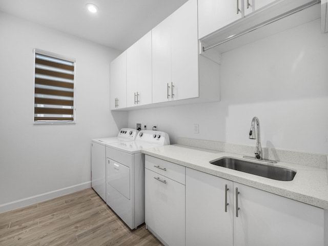 clothes washing area with cabinet space, light wood finished floors, baseboards, washing machine and dryer, and a sink