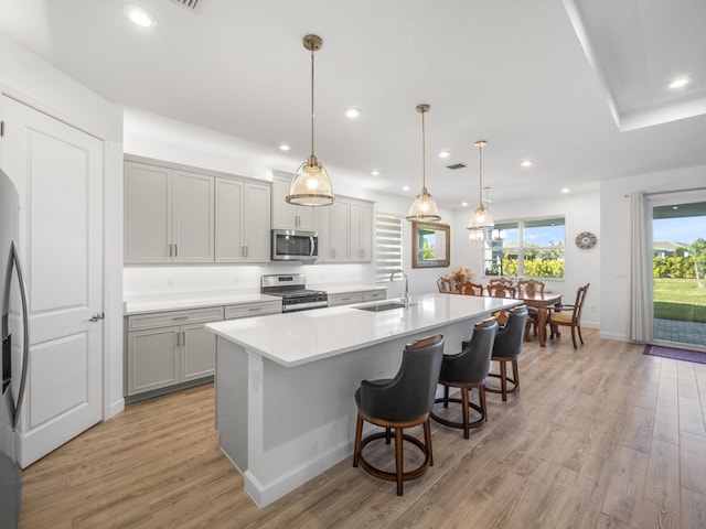 kitchen featuring sink, light hardwood / wood-style floors, decorative light fixtures, a kitchen island with sink, and appliances with stainless steel finishes