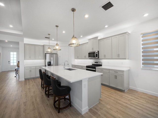 kitchen featuring sink, light hardwood / wood-style floors, a breakfast bar, a center island with sink, and appliances with stainless steel finishes