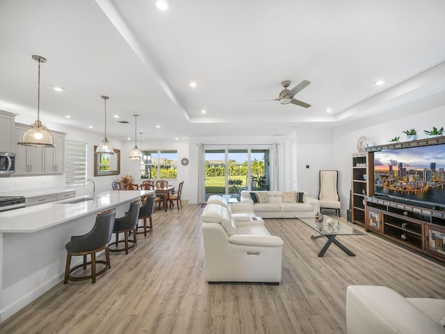 living room with ceiling fan, a raised ceiling, light wood-type flooring, and sink