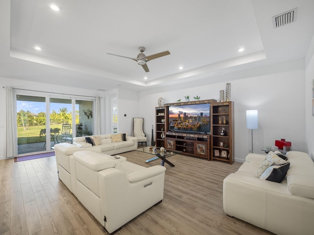 living room with ceiling fan, a raised ceiling, and light hardwood / wood-style flooring