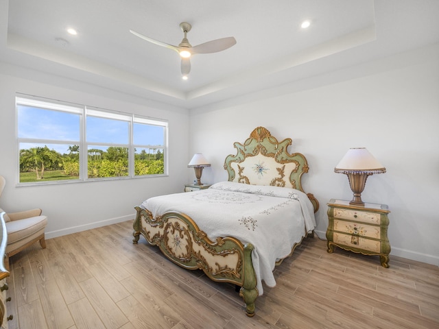 bedroom featuring light wood-type flooring, a raised ceiling, and ceiling fan