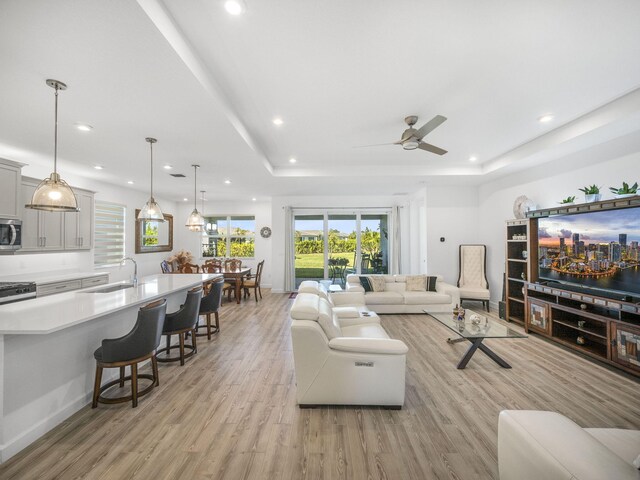 living room featuring light wood finished floors, ceiling fan, a raised ceiling, and recessed lighting