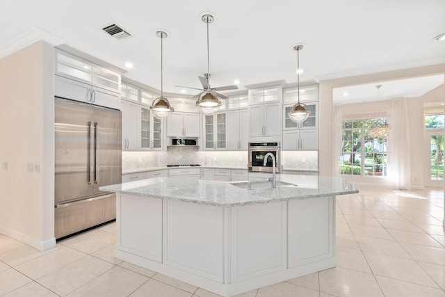 kitchen featuring stainless steel appliances, a kitchen island with sink, backsplash, and decorative light fixtures