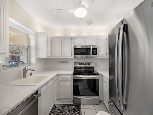 kitchen with stainless steel appliances, ceiling fan, sink, light tile patterned floors, and white cabinetry