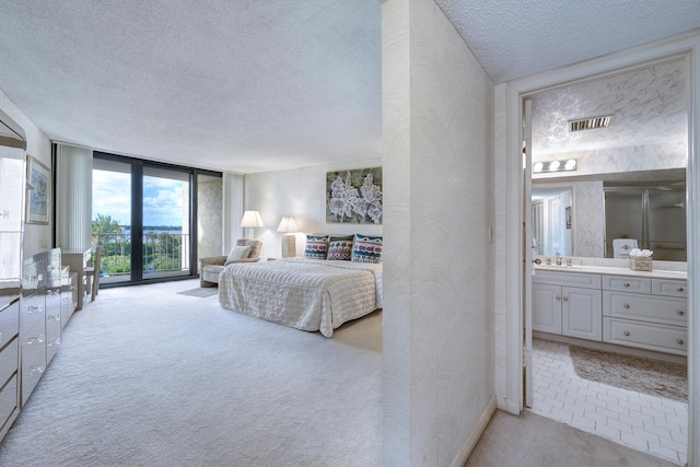 carpeted bedroom with ensuite bath, expansive windows, a textured ceiling, access to outside, and sink