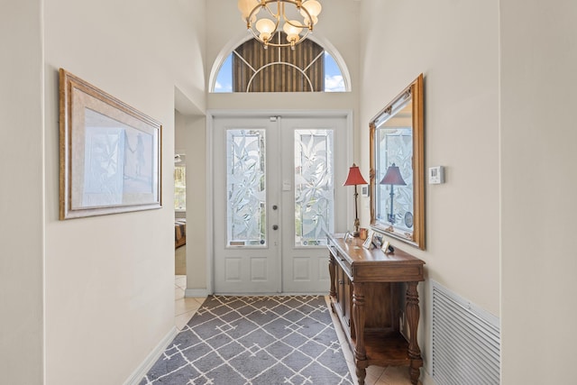 foyer with french doors, a towering ceiling, plenty of natural light, and a notable chandelier