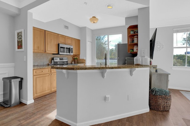 kitchen featuring light wood-type flooring, stainless steel appliances, plenty of natural light, and a breakfast bar area