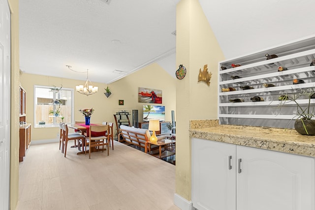 dining space featuring a notable chandelier, light hardwood / wood-style floors, a textured ceiling, and vaulted ceiling