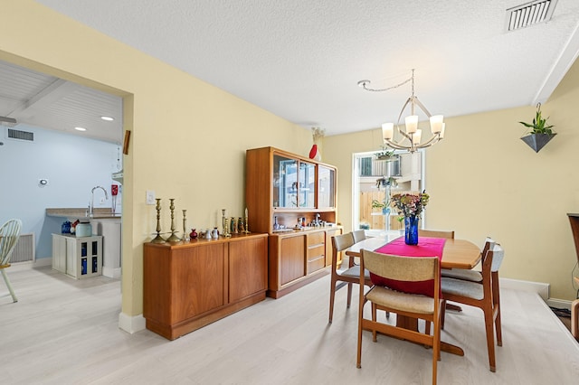 dining room featuring sink, an inviting chandelier, a textured ceiling, and light hardwood / wood-style floors