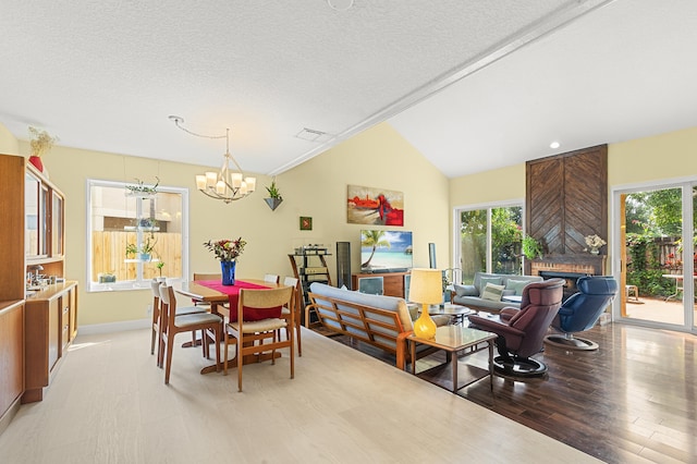 dining space featuring vaulted ceiling, a large fireplace, a notable chandelier, a textured ceiling, and light hardwood / wood-style flooring