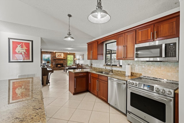 kitchen with appliances with stainless steel finishes, light stone counters, sink, a fireplace, and hanging light fixtures